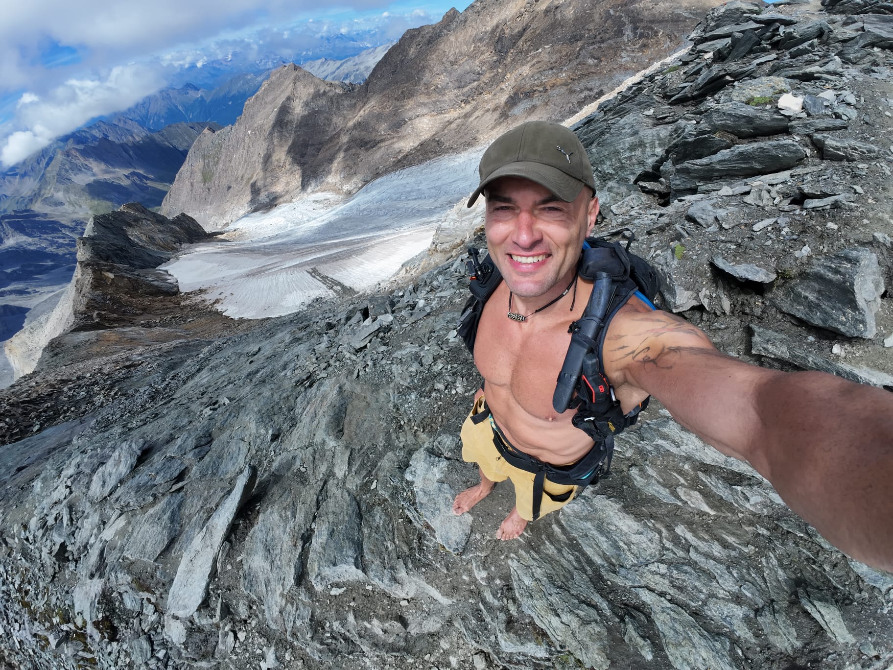 Autoritratto di Claudio Lombardo a piedi nudi su terreno roccioso in alta montagna con il ghiacciaio sullo sfondo