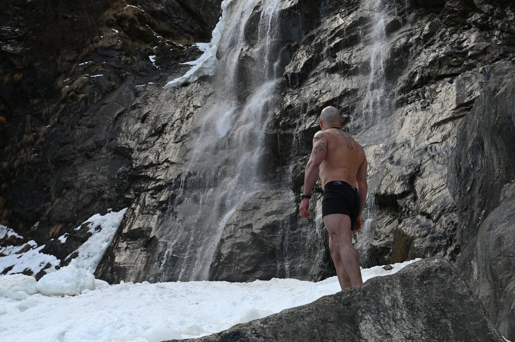 Claudio Lombardo a piedi nudi davanti a una cascata tra rocce e neve