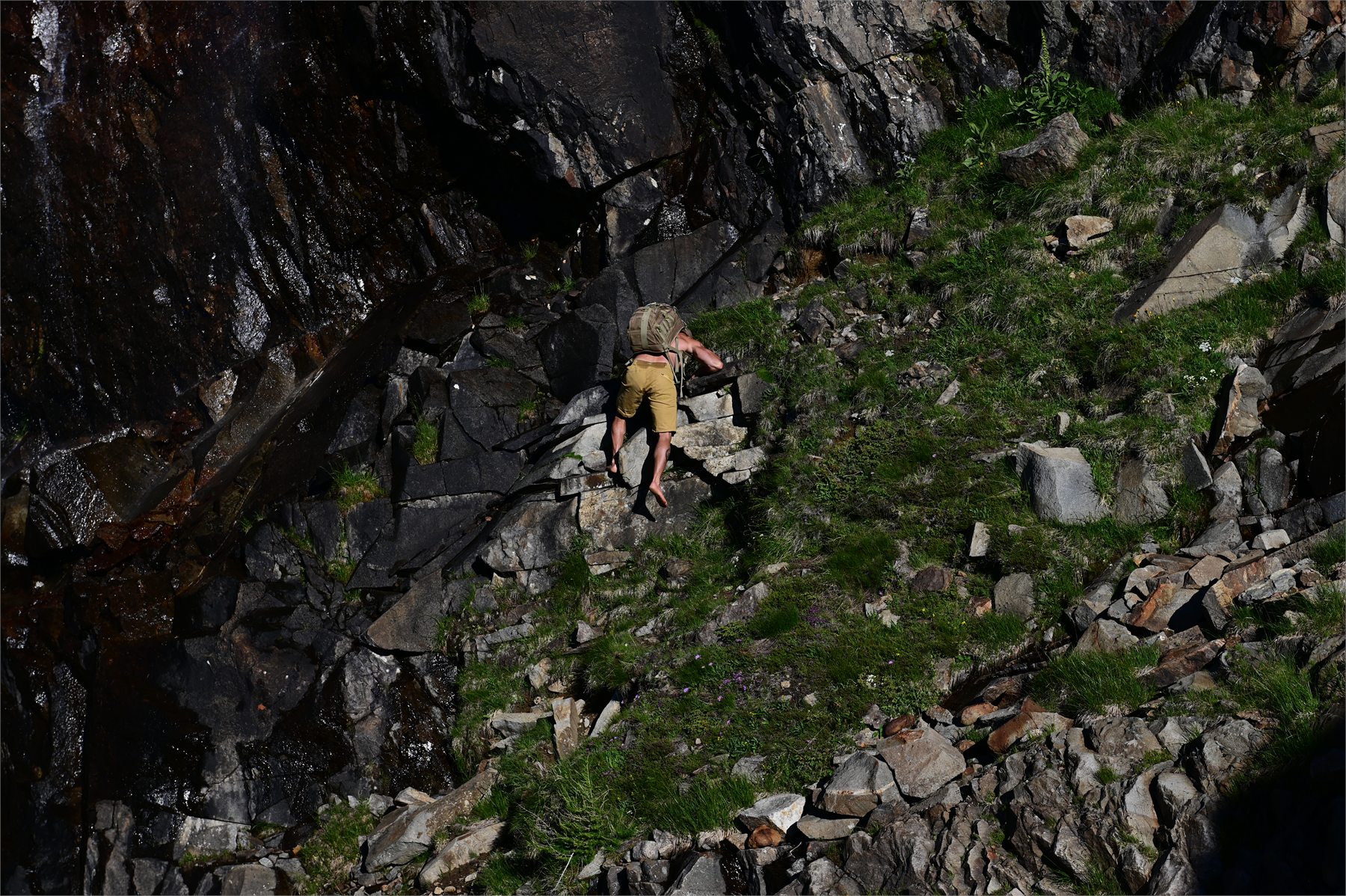 Claudio Lombardo percorre a piedi nudi un tratto alpino tra roccia scura e vegetazione
