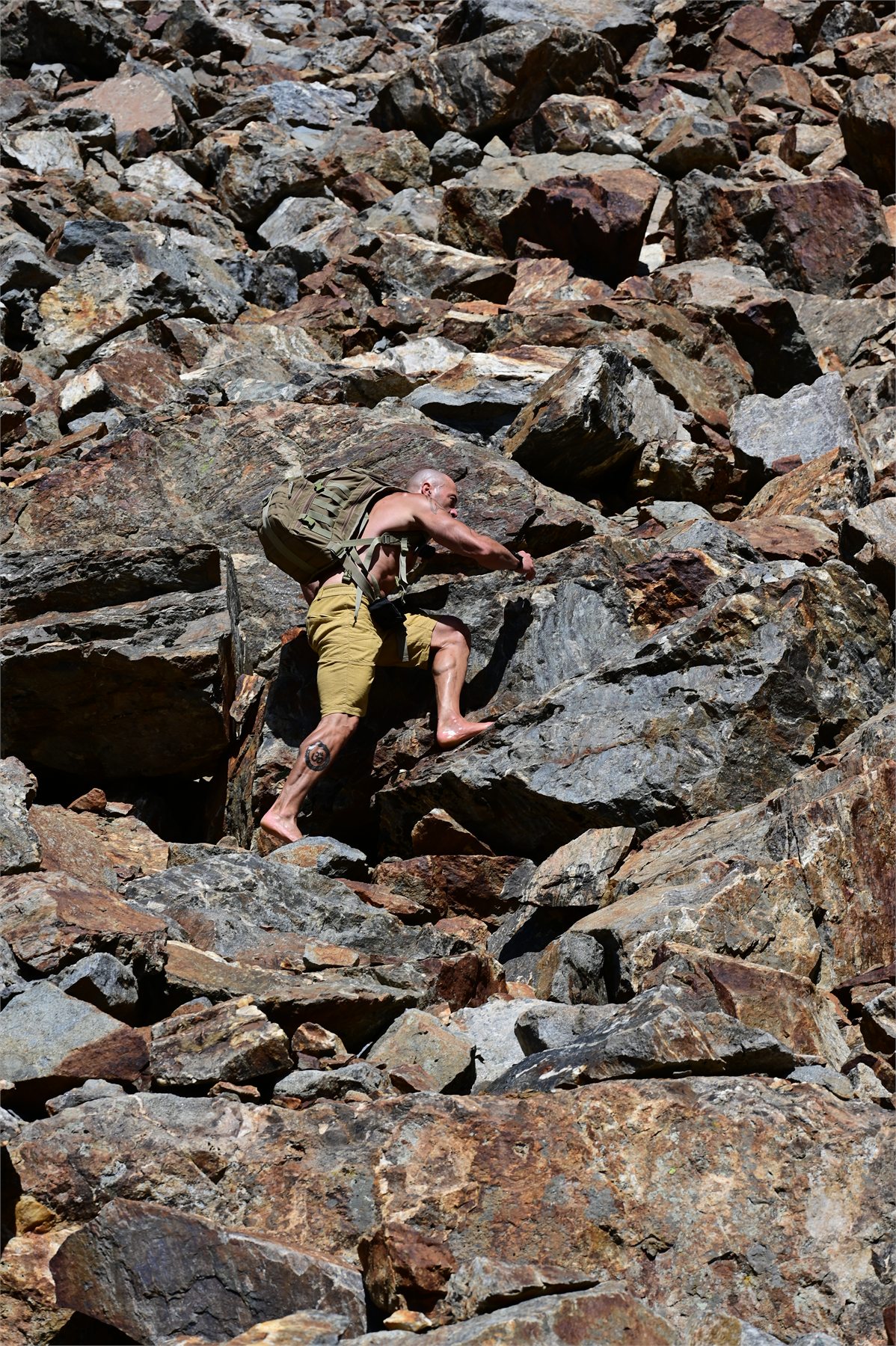 Claudio Lombardo arrampica a piedi nudi tra grandi massi con lo zaino da montagna