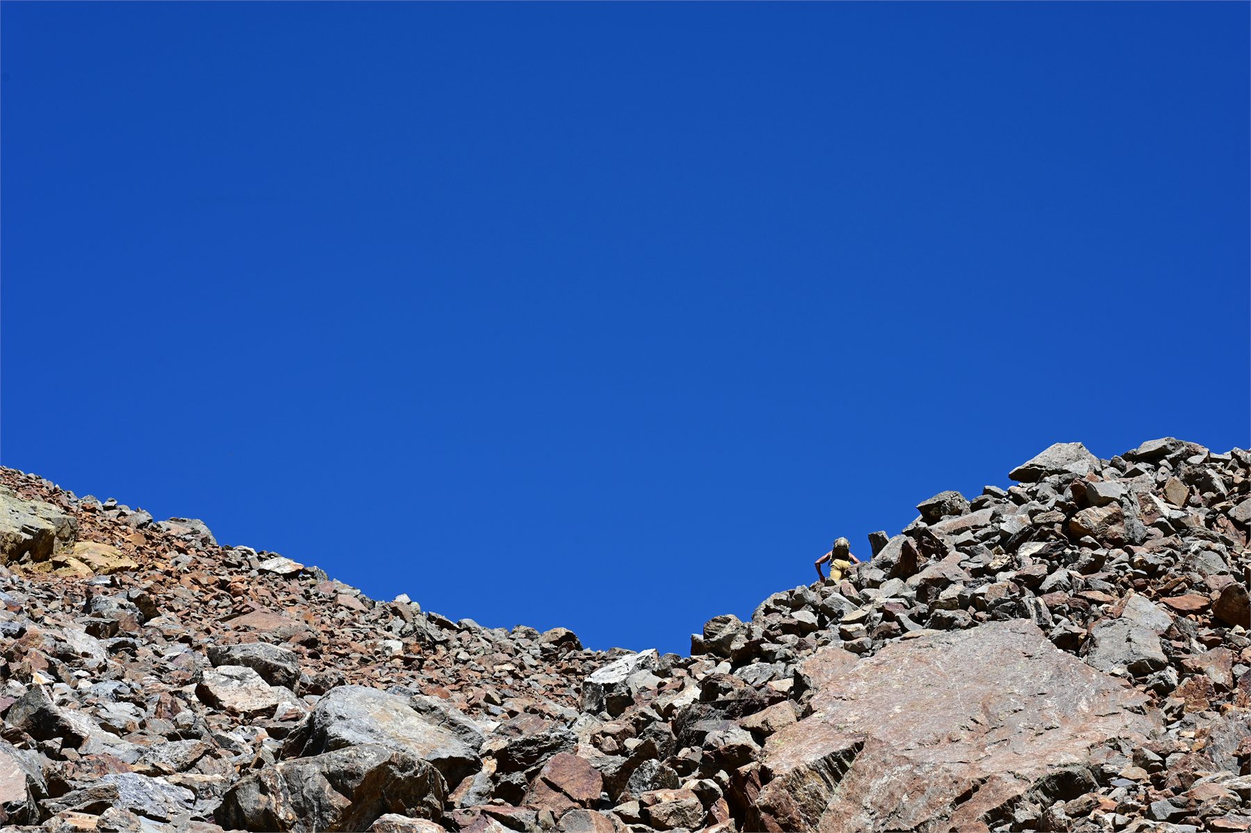 Claudio Lombardo avanza tra le rocce in alta quota sotto un ampio cielo blu
