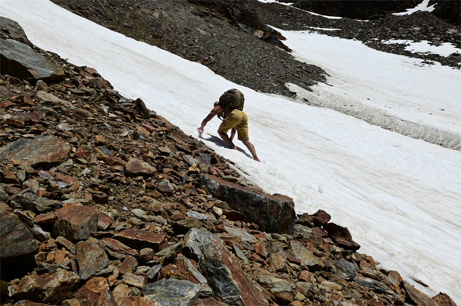 Claudio Lombardo attraversa a piedi nudi un nevaio inclinato accanto alla pietraia