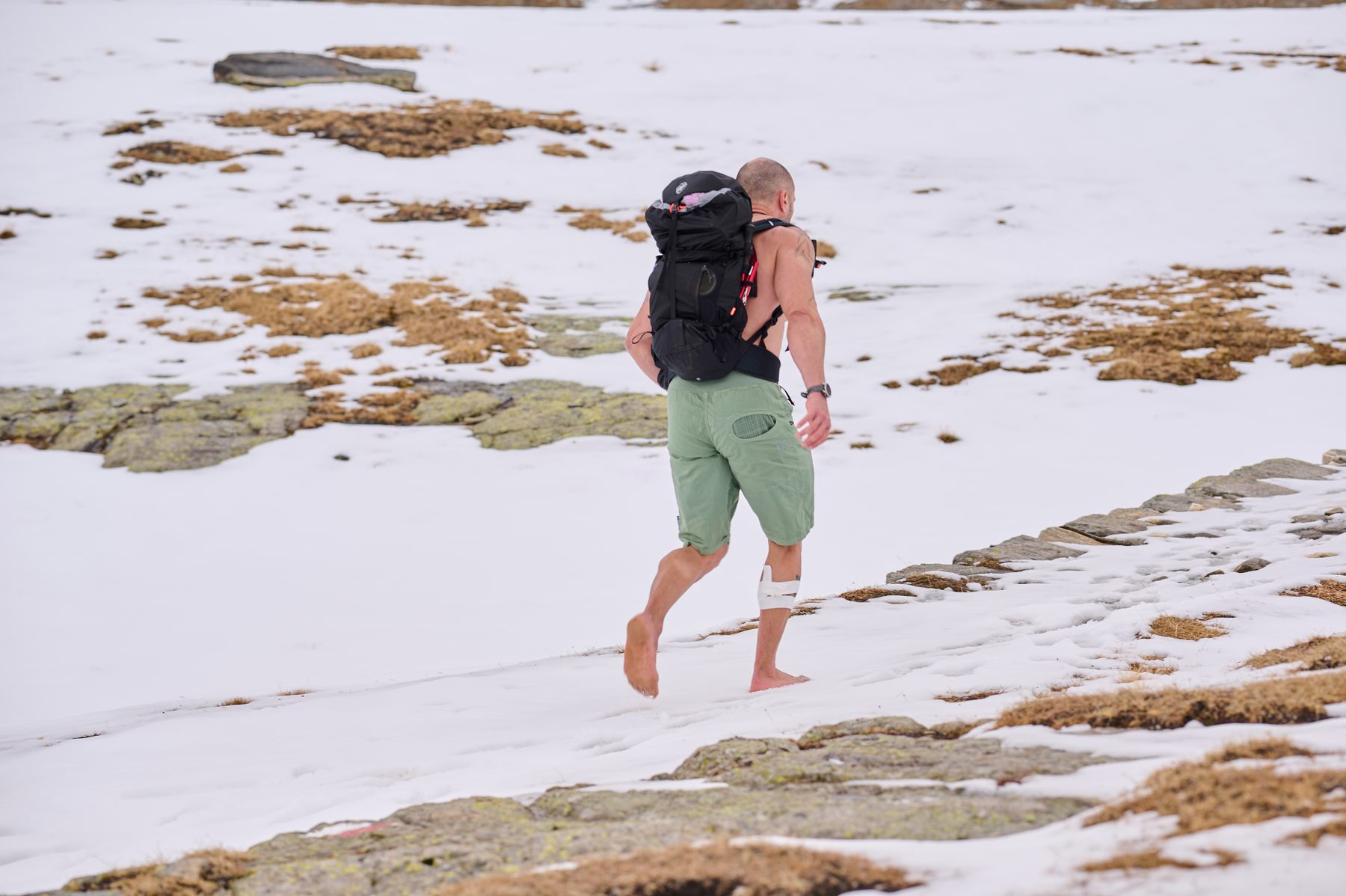 Claudio Lombardo attraversa a piedi nudi un nevaio con lo zaino da montagna