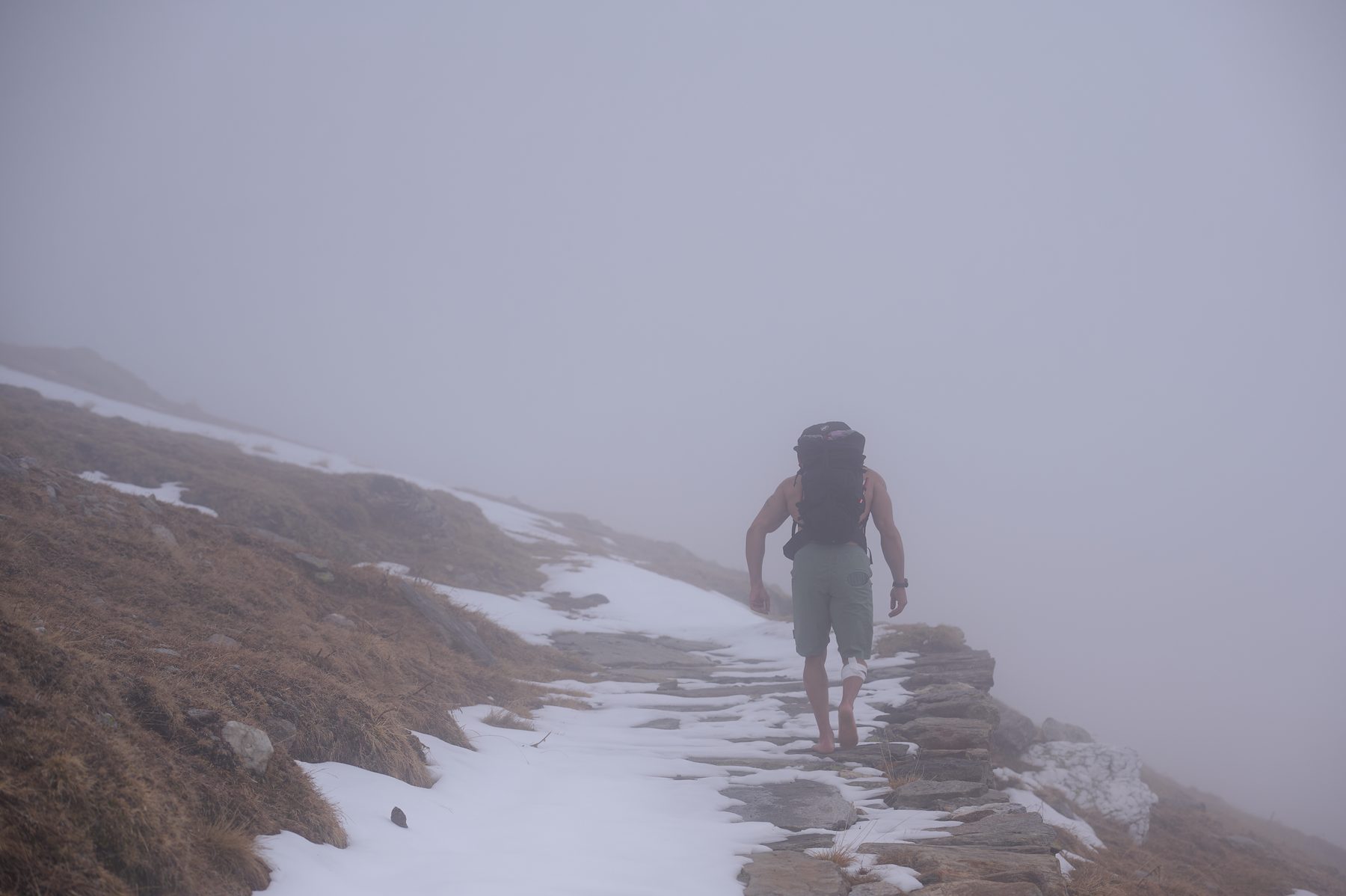Claudio Lombardo cammina con lo zaino su un sentiero di montagna avvolto dalla nebbia