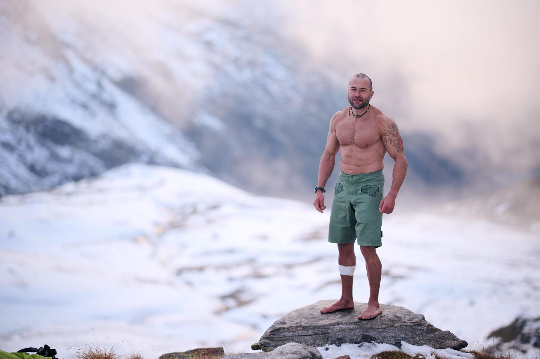 Ritratto di Claudio Lombardo a piedi nudi su una roccia con la neve sullo sfondo